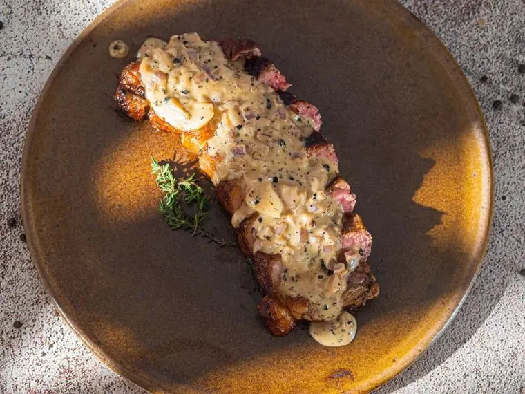 Bife com molho cremoso de pimenta e tomilho em prato ocre