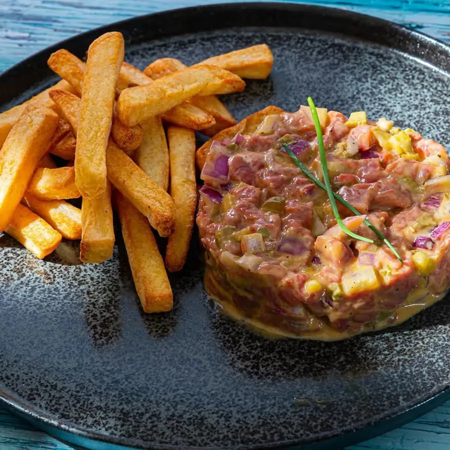 Steak tartare com fritas em prato escuro