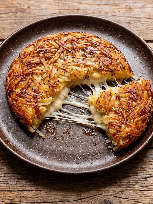 Batata rösti dourada partida ao meio, com queijo derretido, em prato escuro