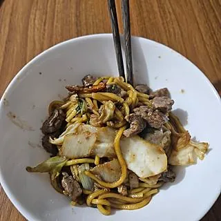 Yakisoba de carne com repolho em tigela branca, com hashis, feito por Andrielly