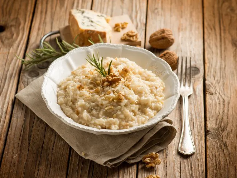 Risoto cremoso com nozes e alecrim em prato branco, com queijo azul ao fundo