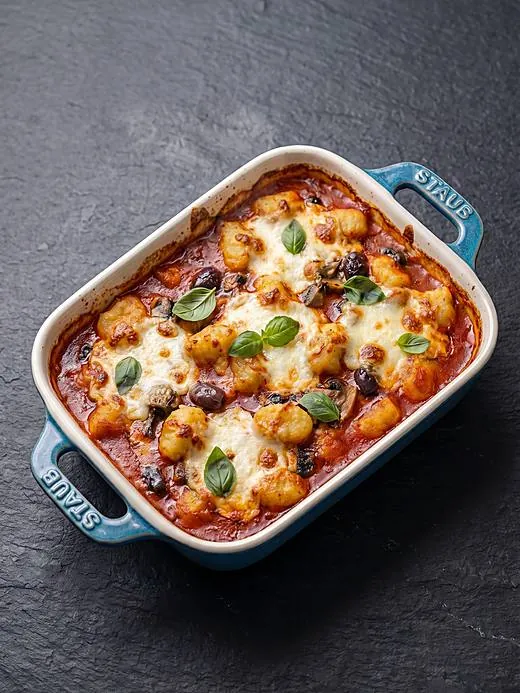 Nhoque gratinado com molho de tomate, muçarela e manjericão em travessa azul