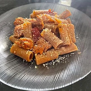 Rigatoni com molho vermelho e queijo ralado em prato de vidro, feito por Larissa Conti