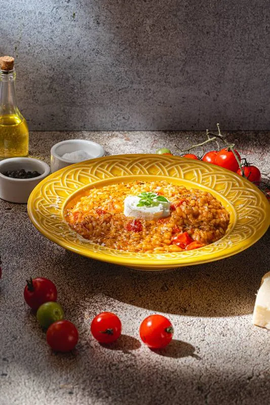 Risoto de cogumelos e ervilhas em prato fundo branco, ao lado de uma taça de vinho branco