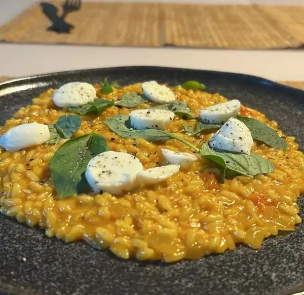 Risoto alaranjado com muçarela de búfala e manjericão em prato escuro, feito por Ricardo
