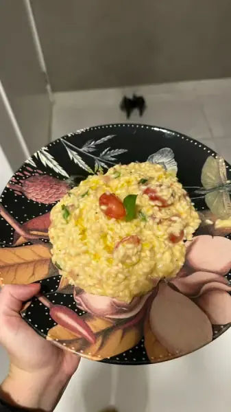 Risoto de parmesão com tomate e manjericão em prato preto estampado, feito por Gabriela Meneguim