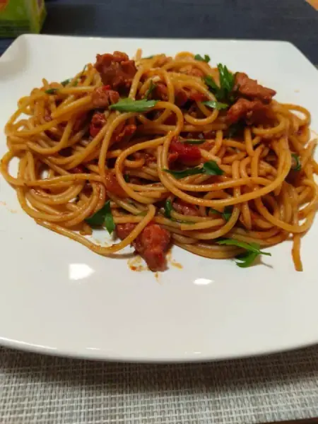 Espaguete ao ragu de linguiça com ervas frescas em prato branco, feito por Daniel Nakamura