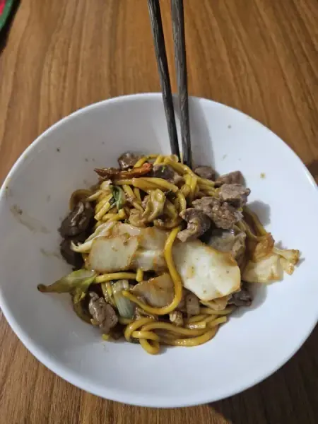 Yakisoba de carne com repolho em tigela branca, com hashis, feito por Andrielly