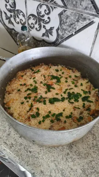 Galinhada com cebolinha em panela grande de alumínio, feita por Denis Magalhães