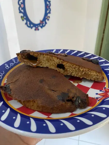 Cookie grande cortado ao meio, recheado de doce de leite, em prato estampado azul e vermelho, feito por Danillo Bueno