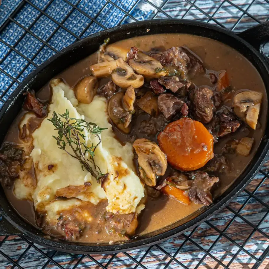 Boeuf bourguignon com cogumelos e cenoura ao lado de purê com tomilho, em frigideira de ferro