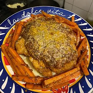 Parmegiana gratinada cercada de palitos de cenoura, em prato azul e branco, feita por Danillo Bueno