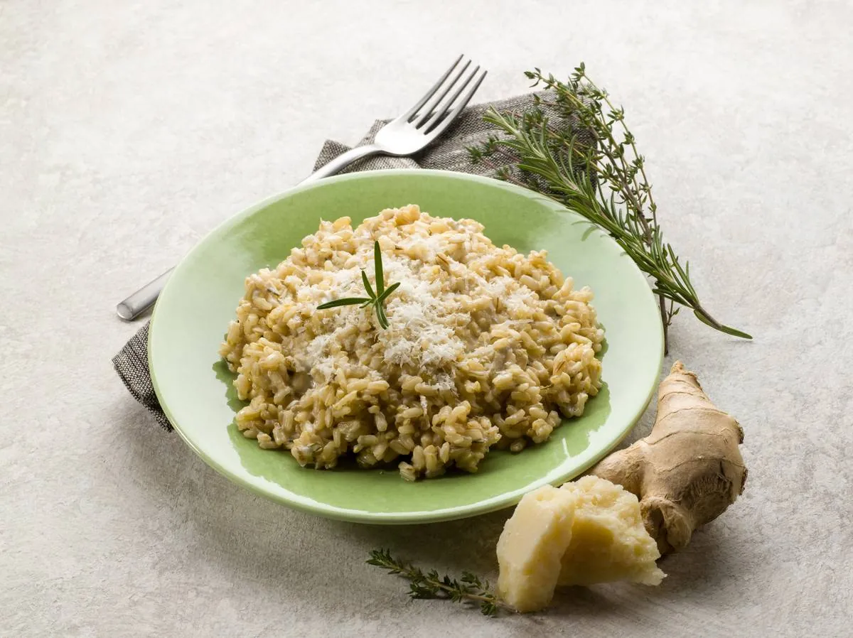 Risoto com parmesão ralado e alecrim em prato verde, com um pedaço de queijo ao lado