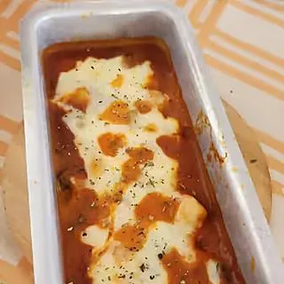 Forma de alumínio com molho de tomate e muçarela derretida, feita por Cass Brandão