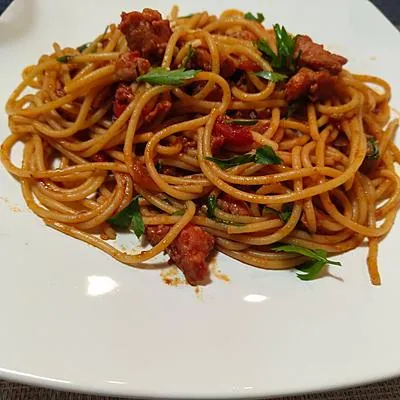 Espaguete ao ragu de linguiça com ervas frescas em prato branco, feito por Daniel Nakamura