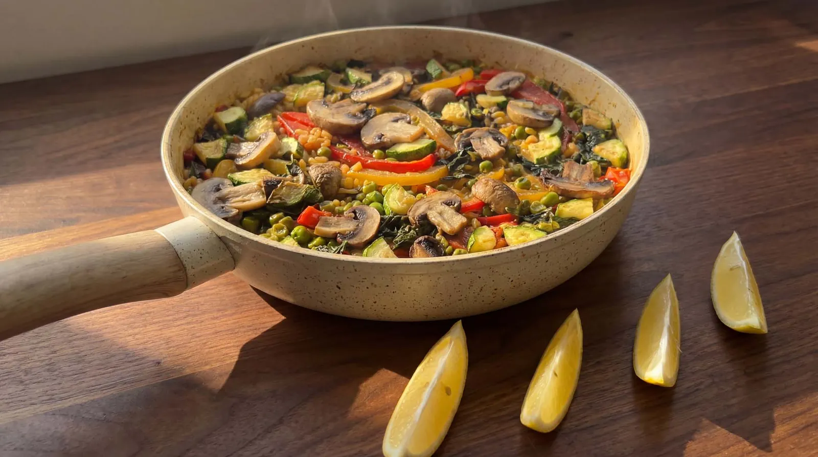 Paella vegetariana com cogumelos e pimentão em frigideira bege, com gomos de limão